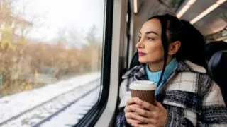 Woman with coffee riding train through snow